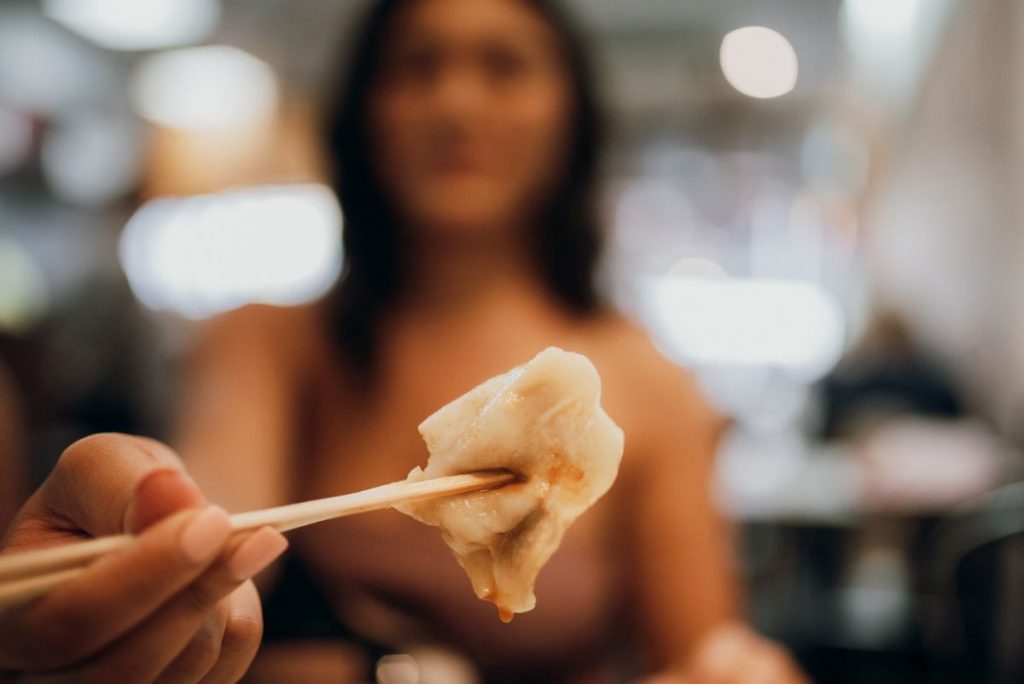 A woman holding a soup dumpling with her chopsticks. 