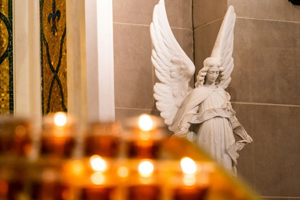 Lit candles near an angel statue. 