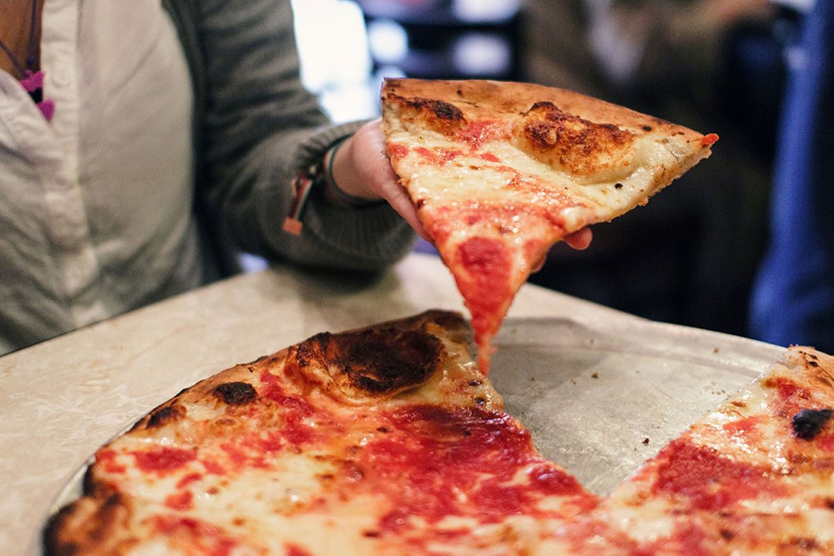 woman pulling slice of pizza from whole pizza pie