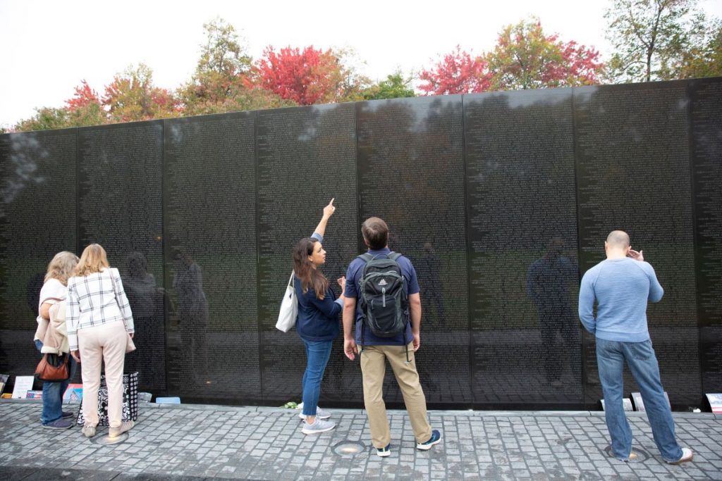 woman pointing to a black wall with names listed on it