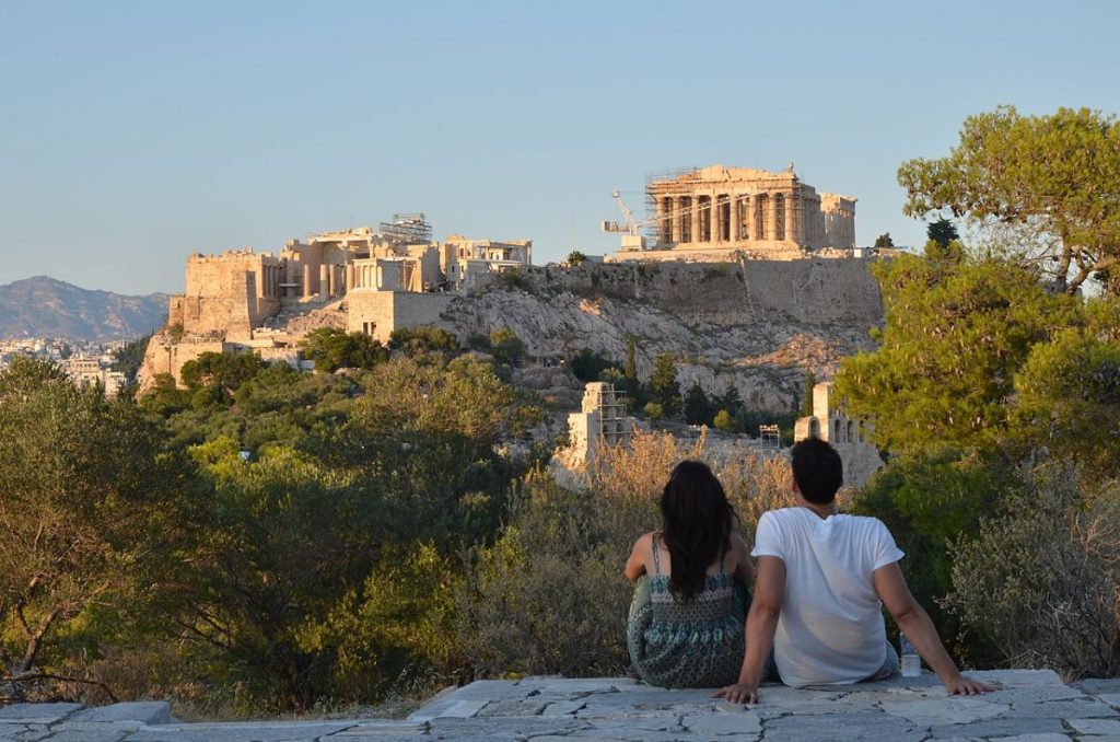 People sitting at Filopappos looking at Greek ruins in Athens.