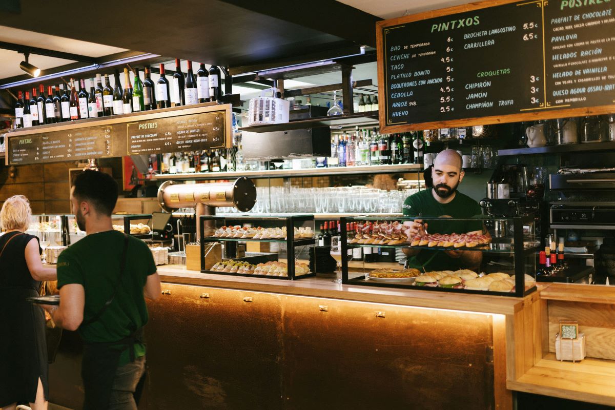 A glass case of pintxos as a server works behind the bar inside a pintxos bar in San Sebastian.