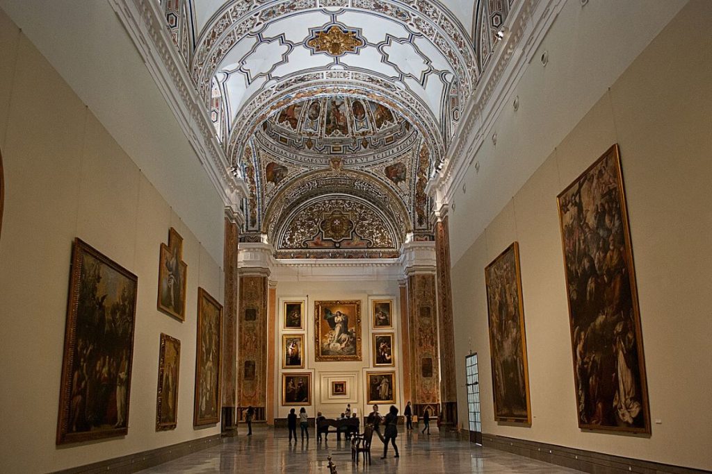 A long hall with paintings and people standing at the end of the hall at Museo de Bellas Artes. 