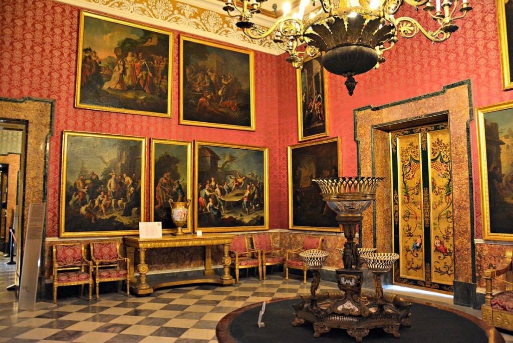A red room with paintings and a chandelier at Palazzo Reale.