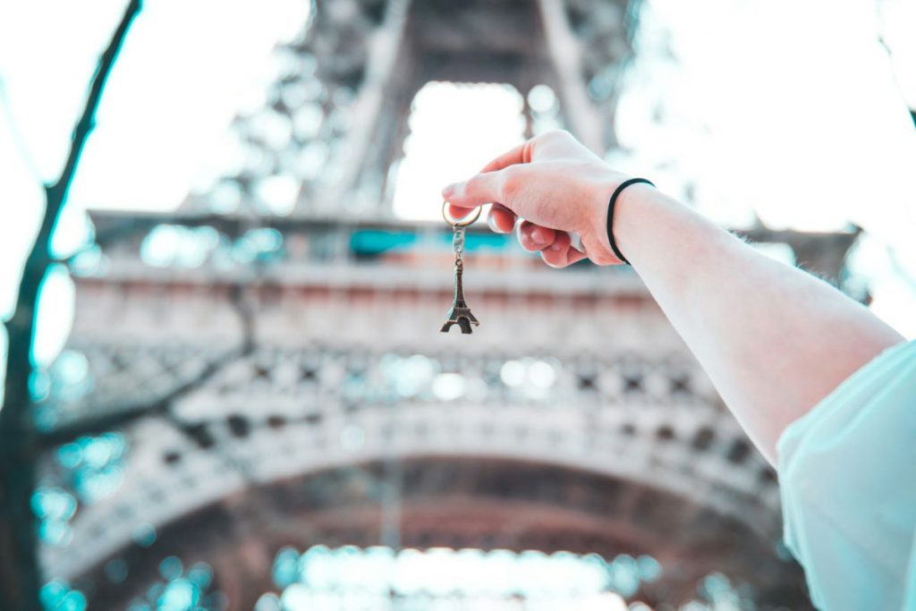 A person holding up a key chain Eiffel Tower in front of the Eiffel Tower in Paris.