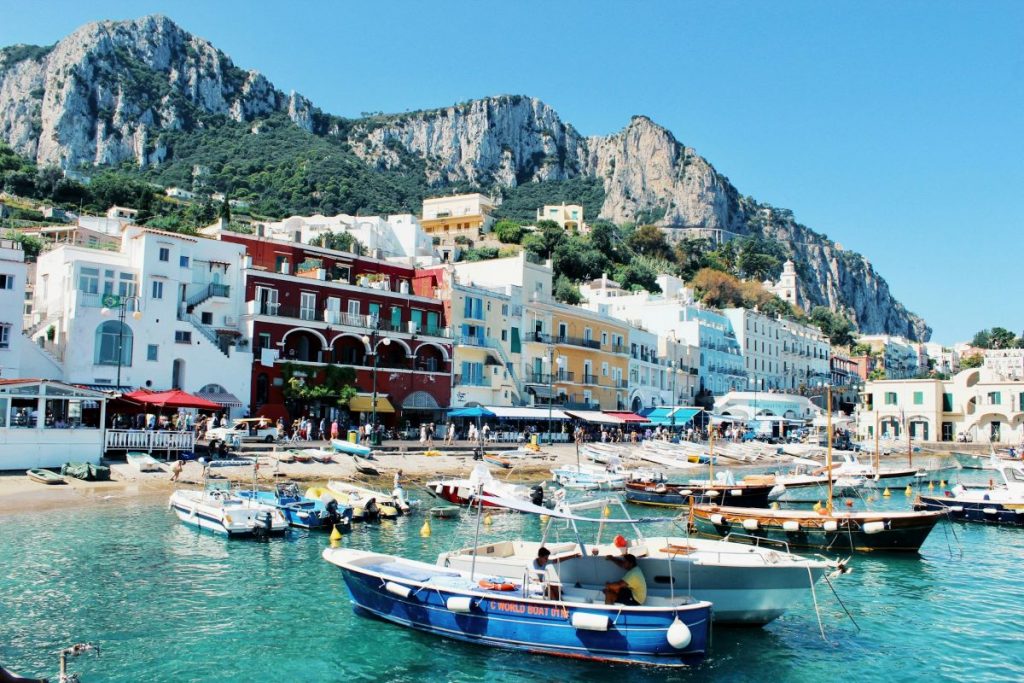 View of Capri, Italy from the ocean. People walking around and boats waiting in the harbor. 