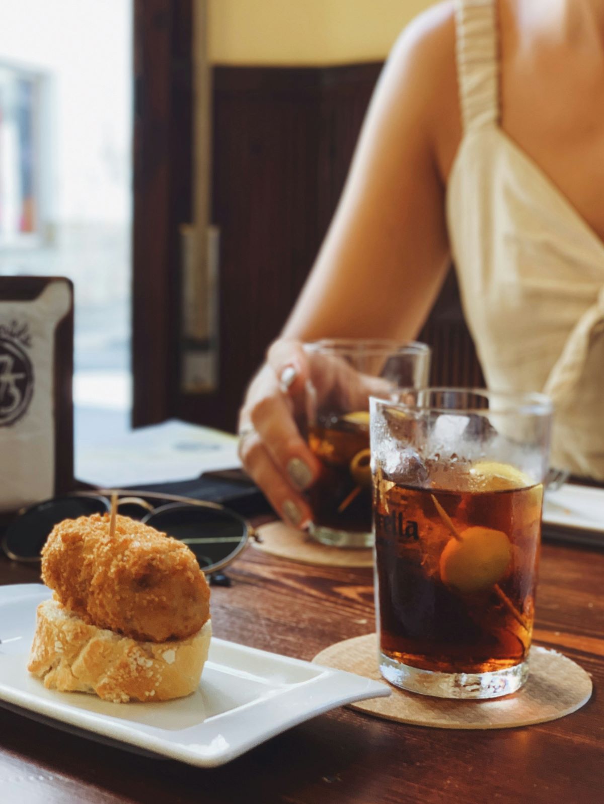 A person eating a croqueta and drinking vermouth at a bar in San Sebastian, Spain.