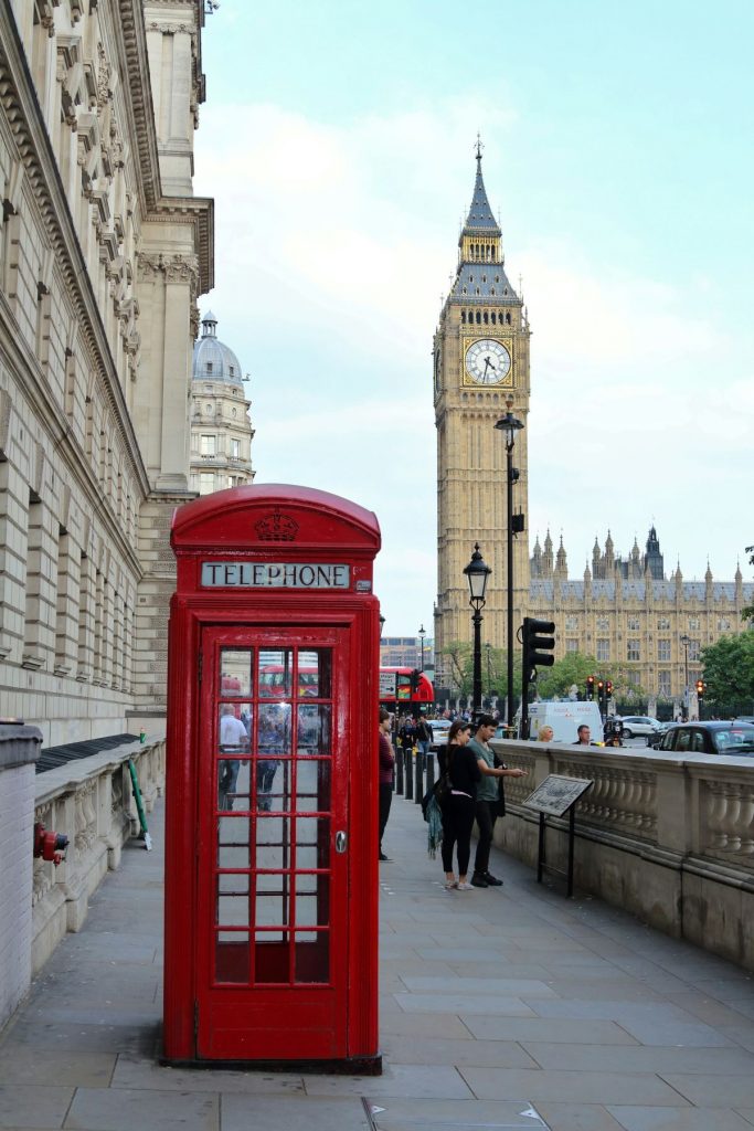 A red telephone booth with people walking by near Big Ben.