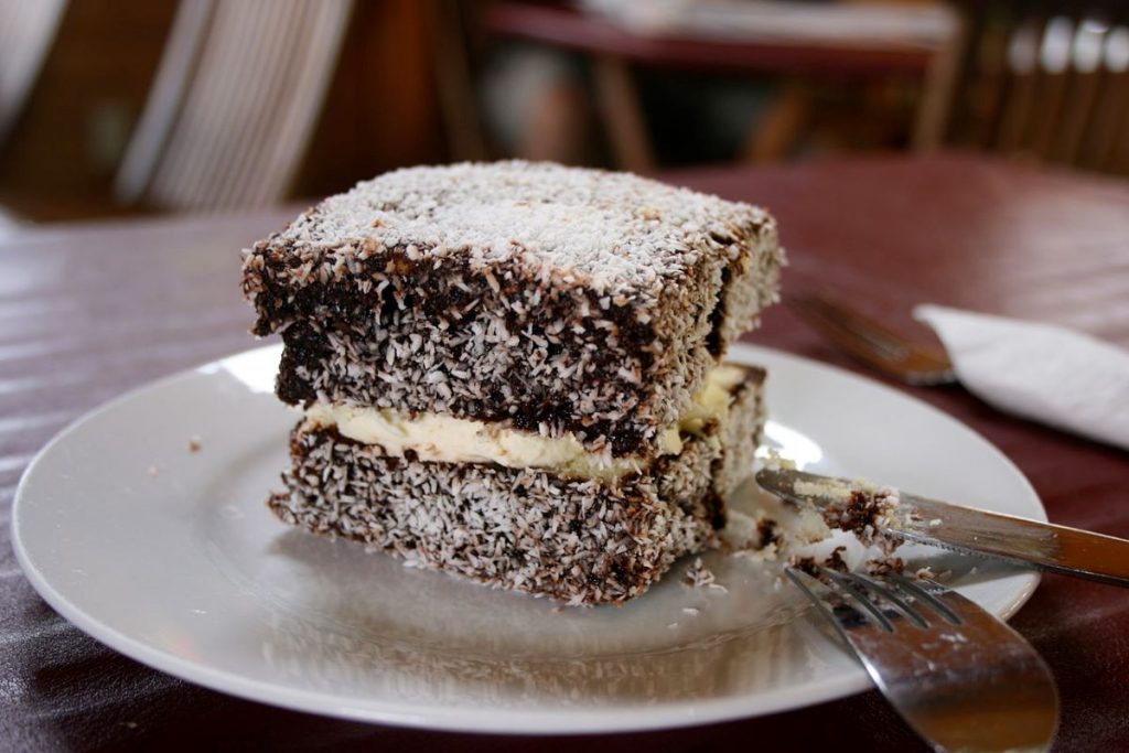 Lamington on a ceramic plate next to a fork and a knife. 