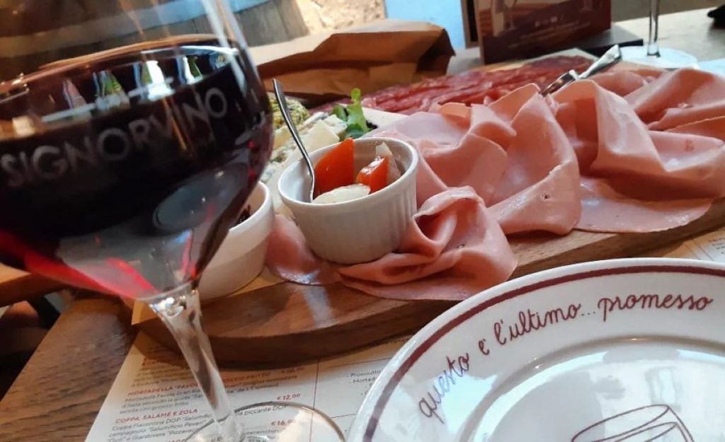 glass of wine on a table in front of charcuterie board with sliced meat