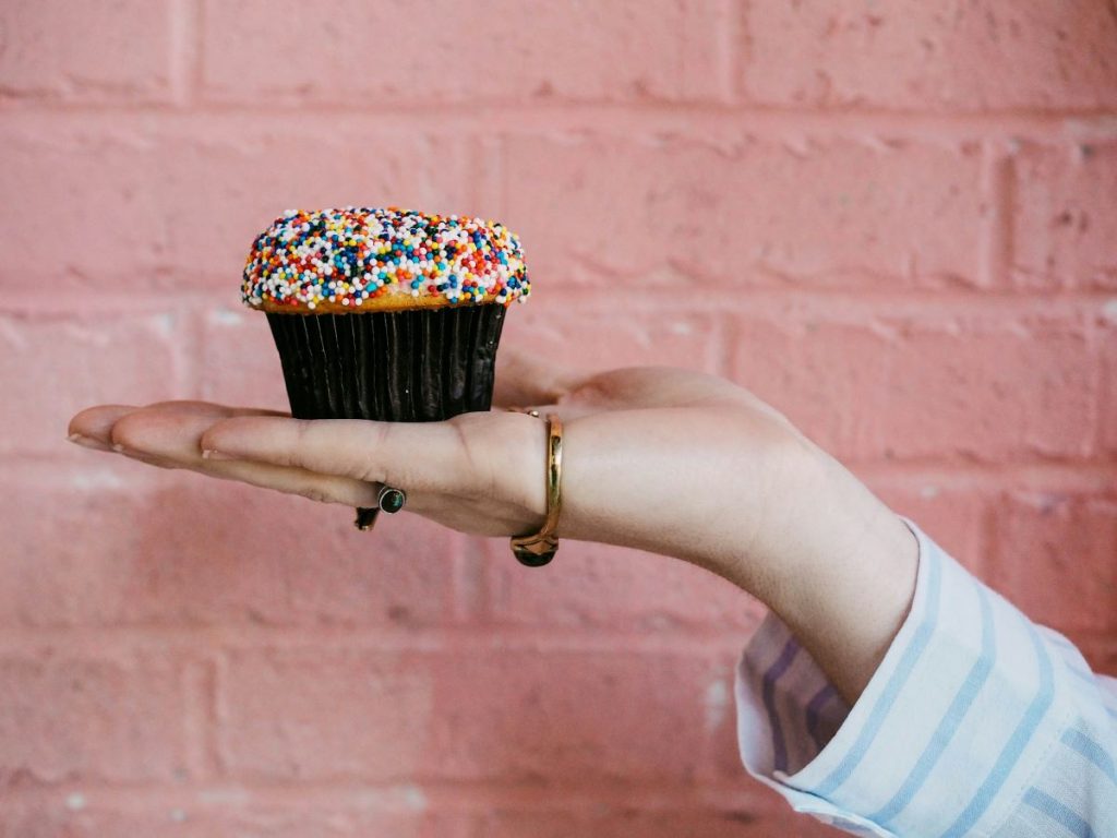 A woman holding a cupcake in front of a pink background. 