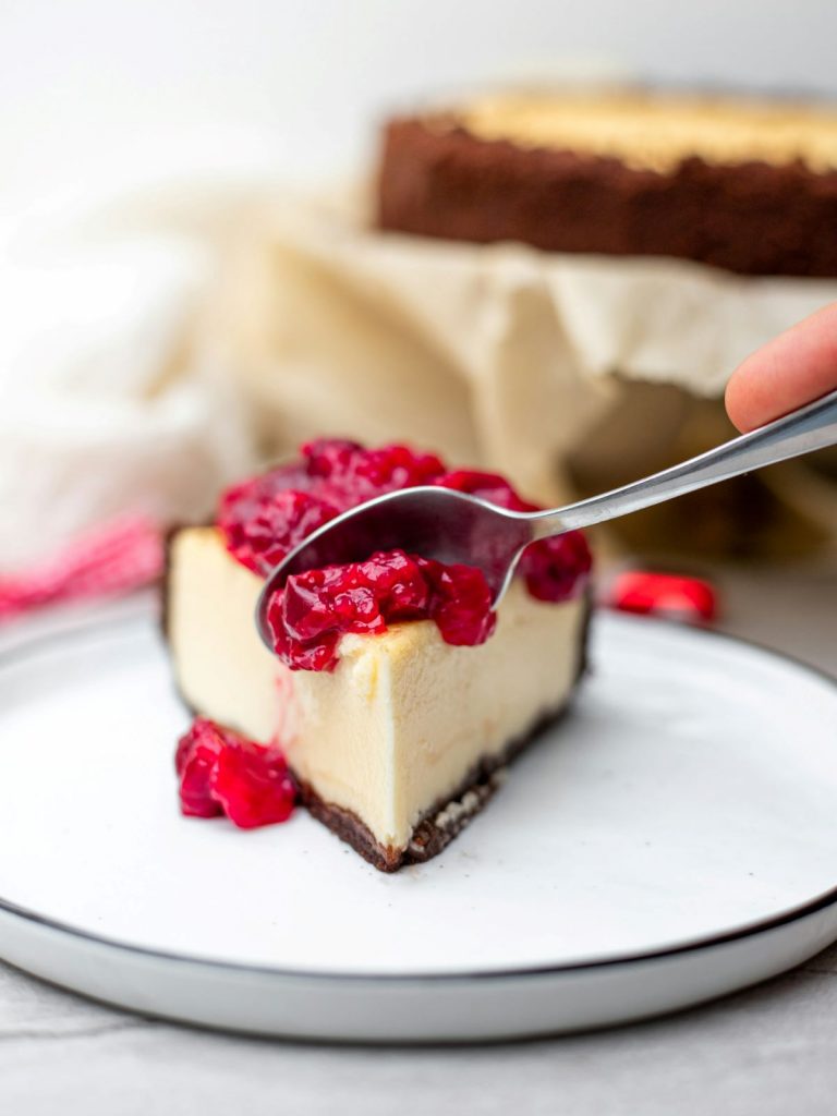 A spoon cutting into a cheesecake topped with raspberry compote. 