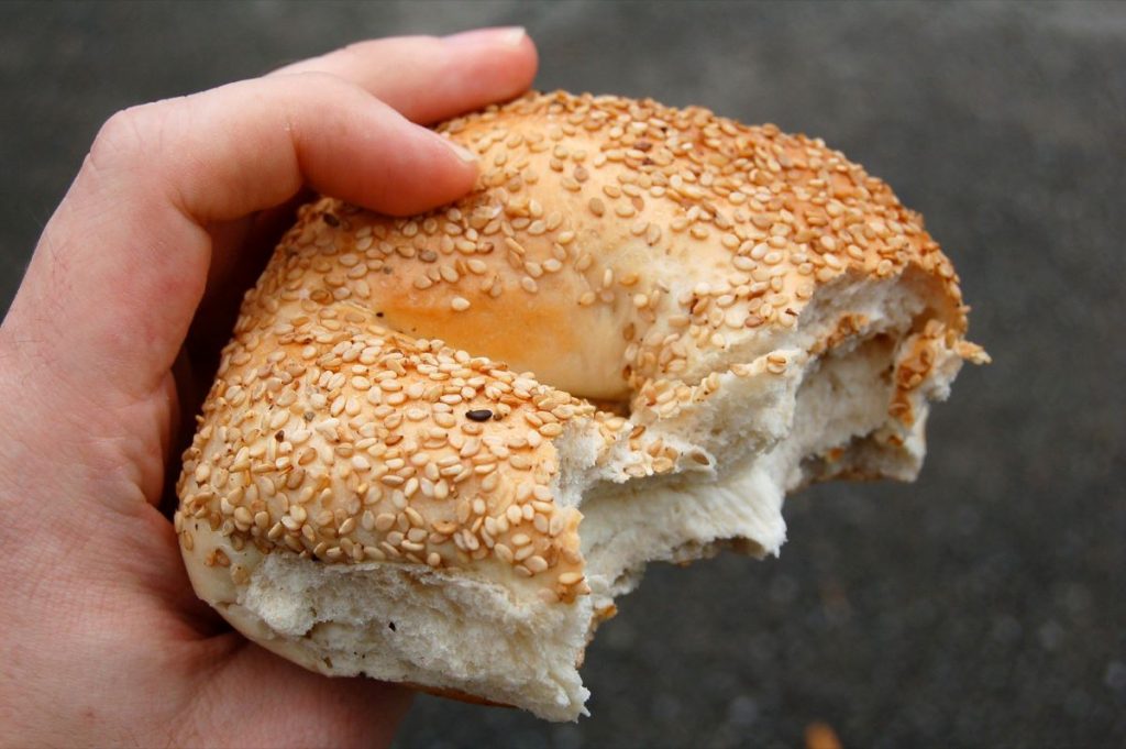 A person holding a sesame bagel with cream cheese. 