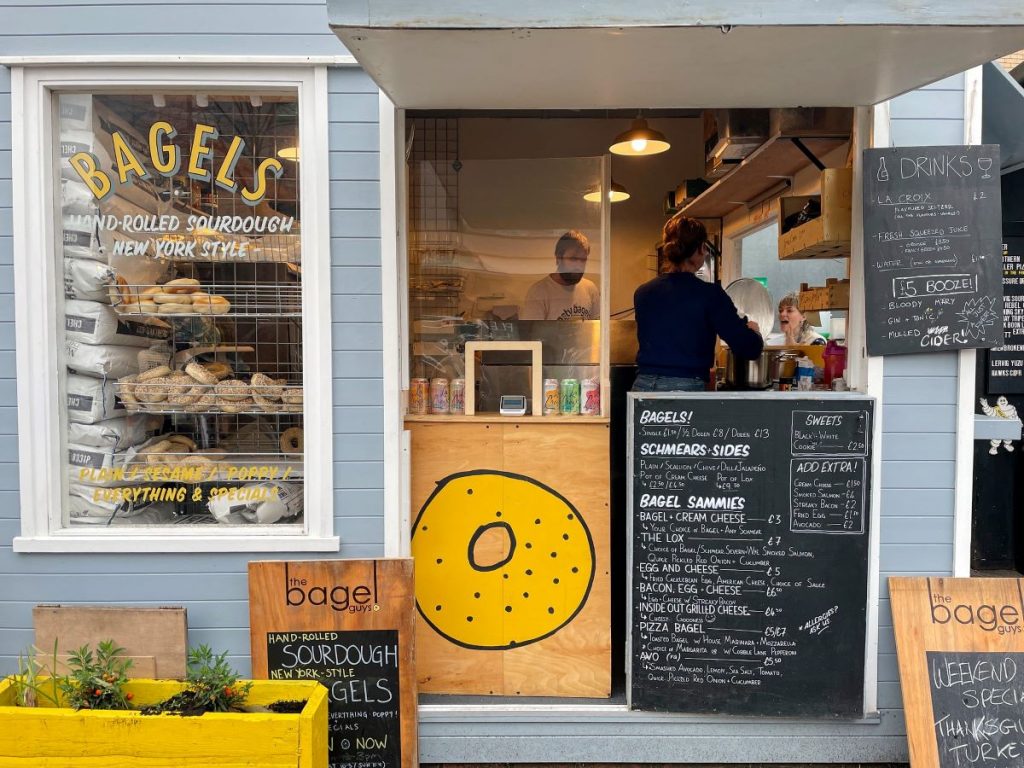 Storefront of The Bagel Guys, one of the best bagels in London, while workers help customers inside. 