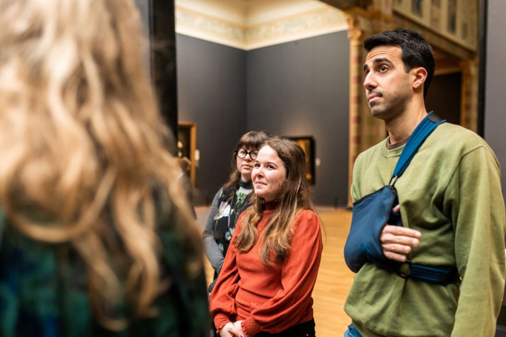 A group of people at the Rijksmuseum looking at a few famous paintings.