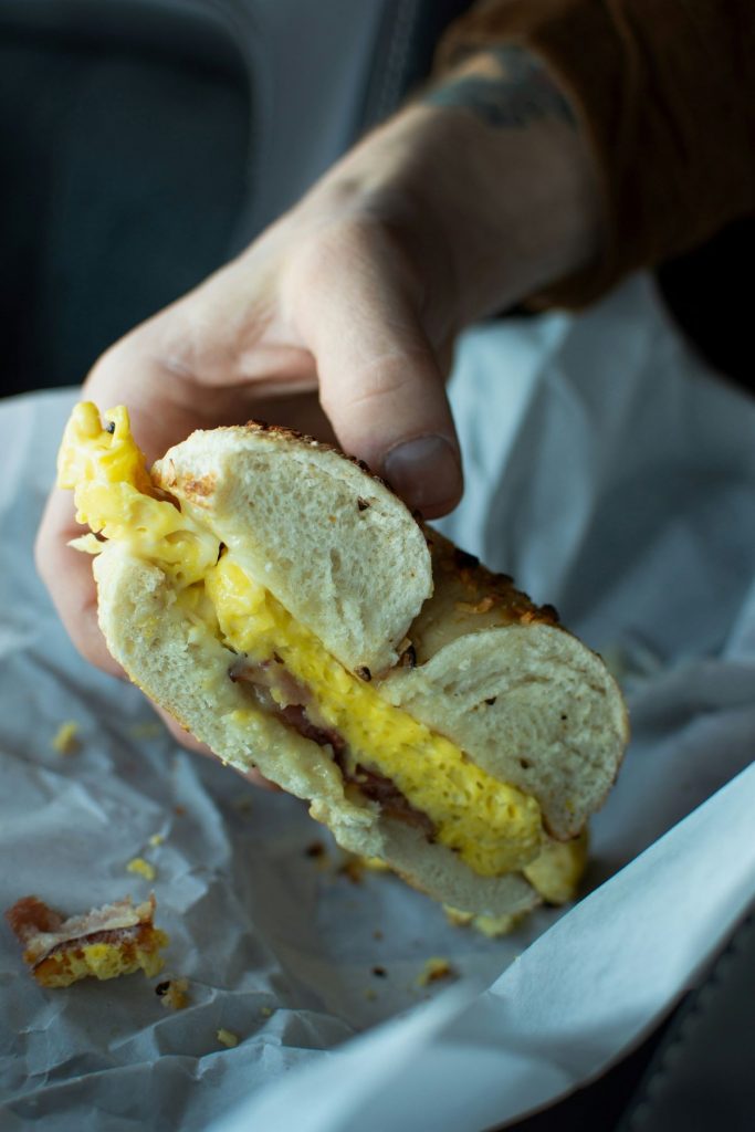 A person holding an egg, bacon, and cheese bagel sandwich. 