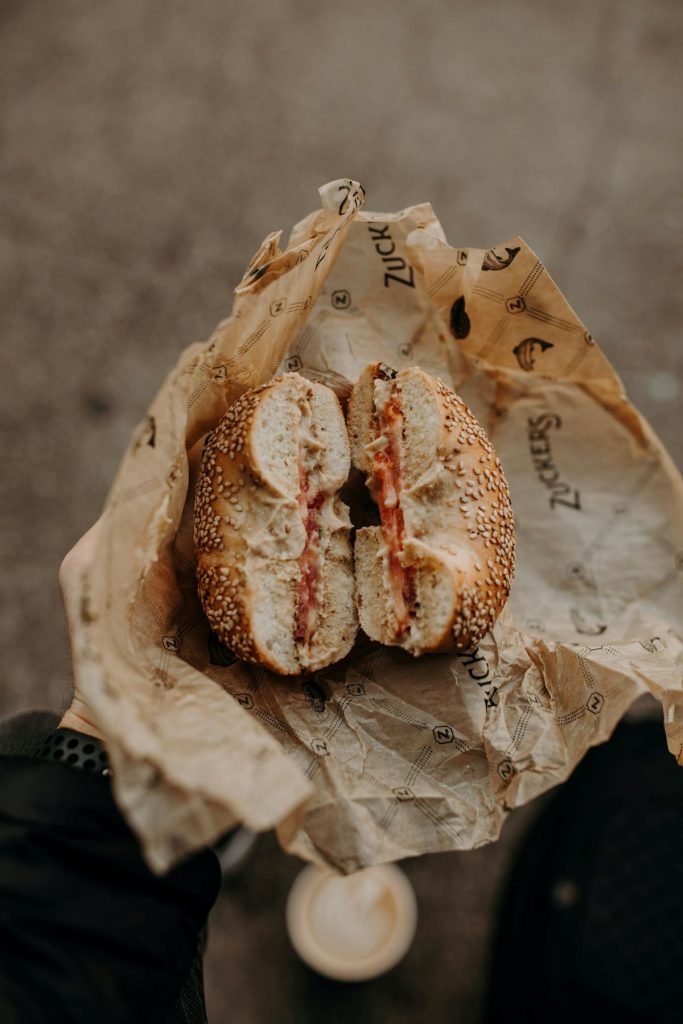 A person holding a bagel sandwich wrapped in paper. 