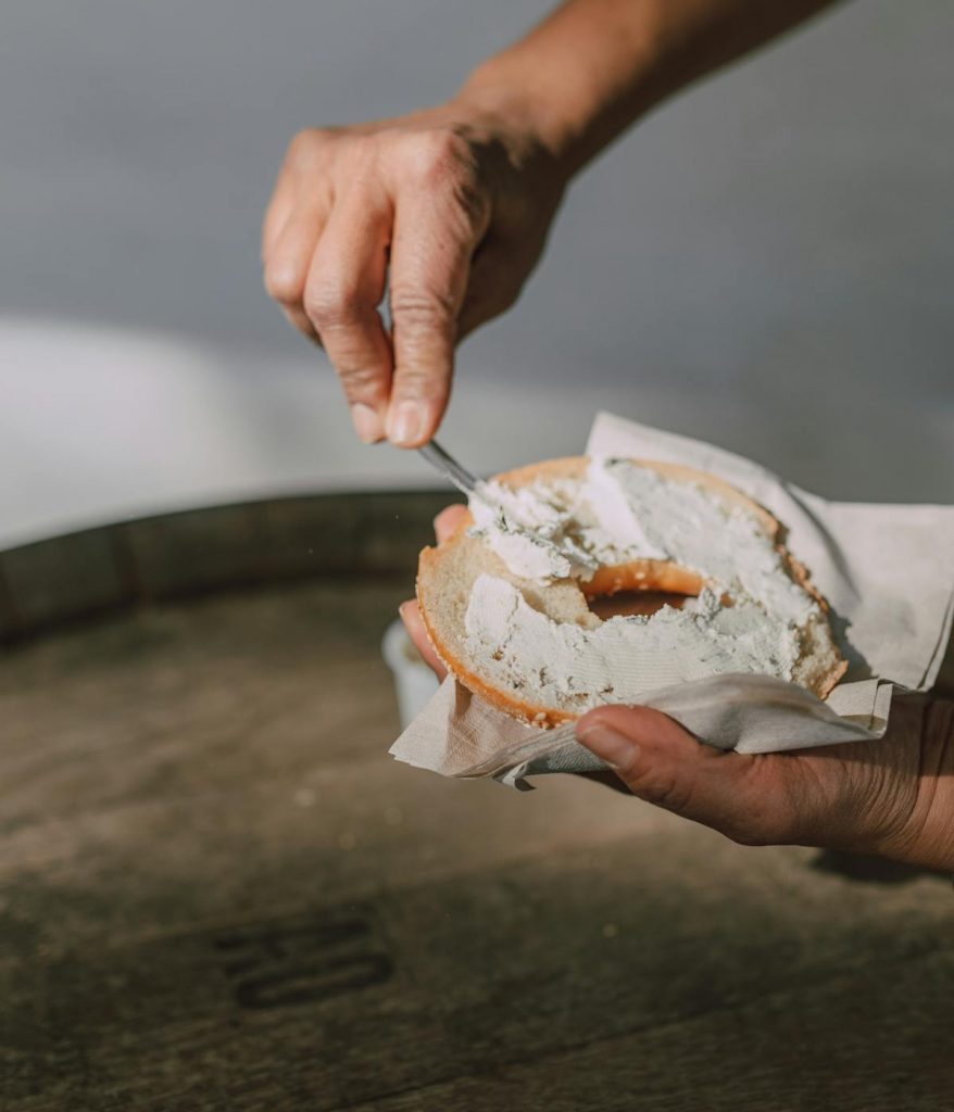 A person spreading cream cheese on a bagel with a knife. 