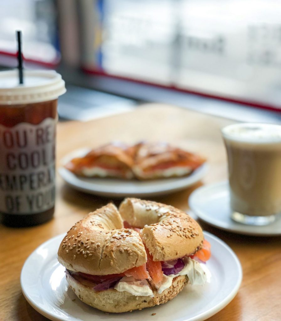 A smoked salmon bagel sandwich on a ceramic plate and coffees. 