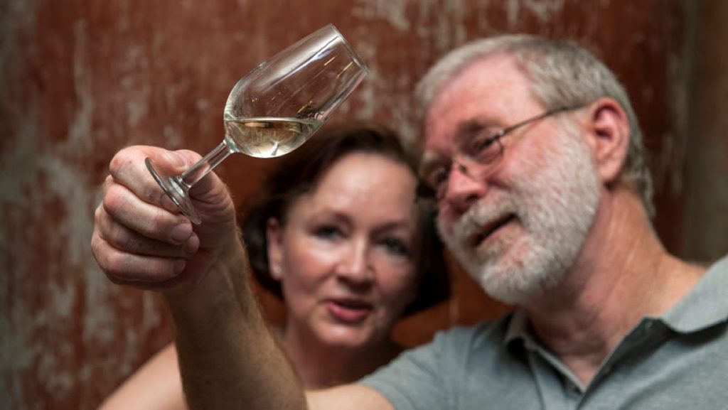 A man and a woman looking at a glass of white sherry wine. 