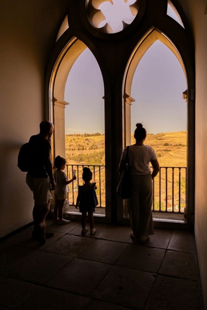 A family looking out the windows of a medieval castle at views of a Spanish city. 