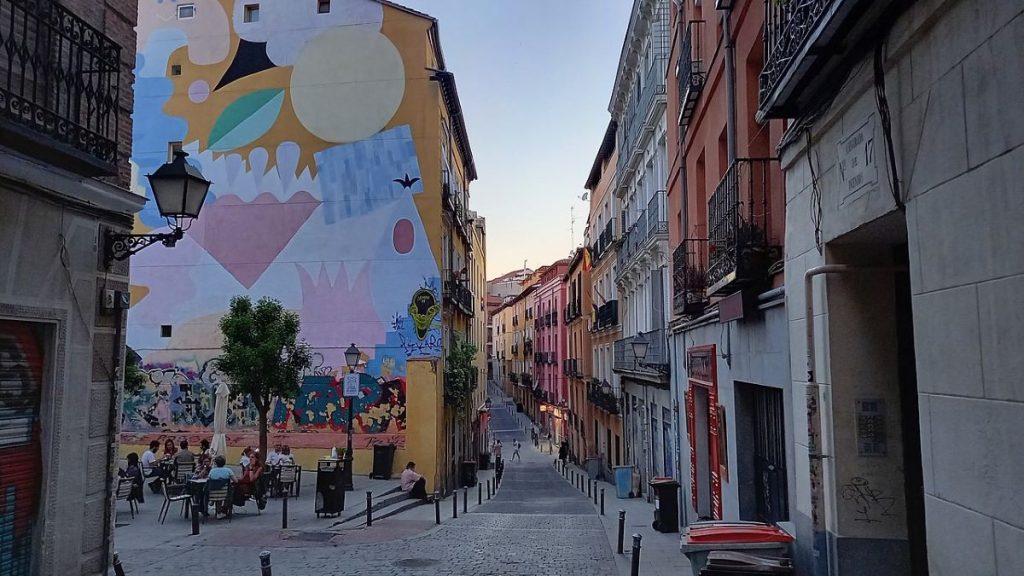 People sitting at an outdoor restaurant in front of a mural in Lavapiés.  