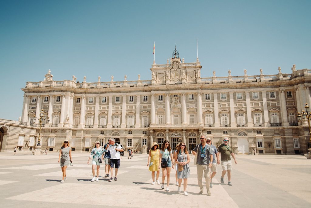 A group of people walking outside of the Royal Palace in Madrid.