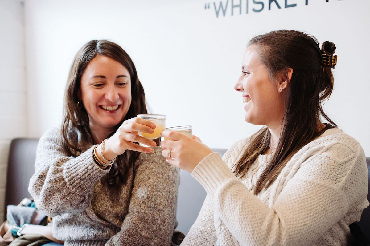 Two women toasting with a whiskey cocktail in a distillery