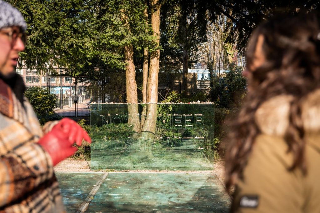 Two people talking in front of a Holocaust memorial in the Amsterdam Jewish Quarter.