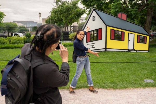 a woman taking a photo of another woman in front of a colorful house.