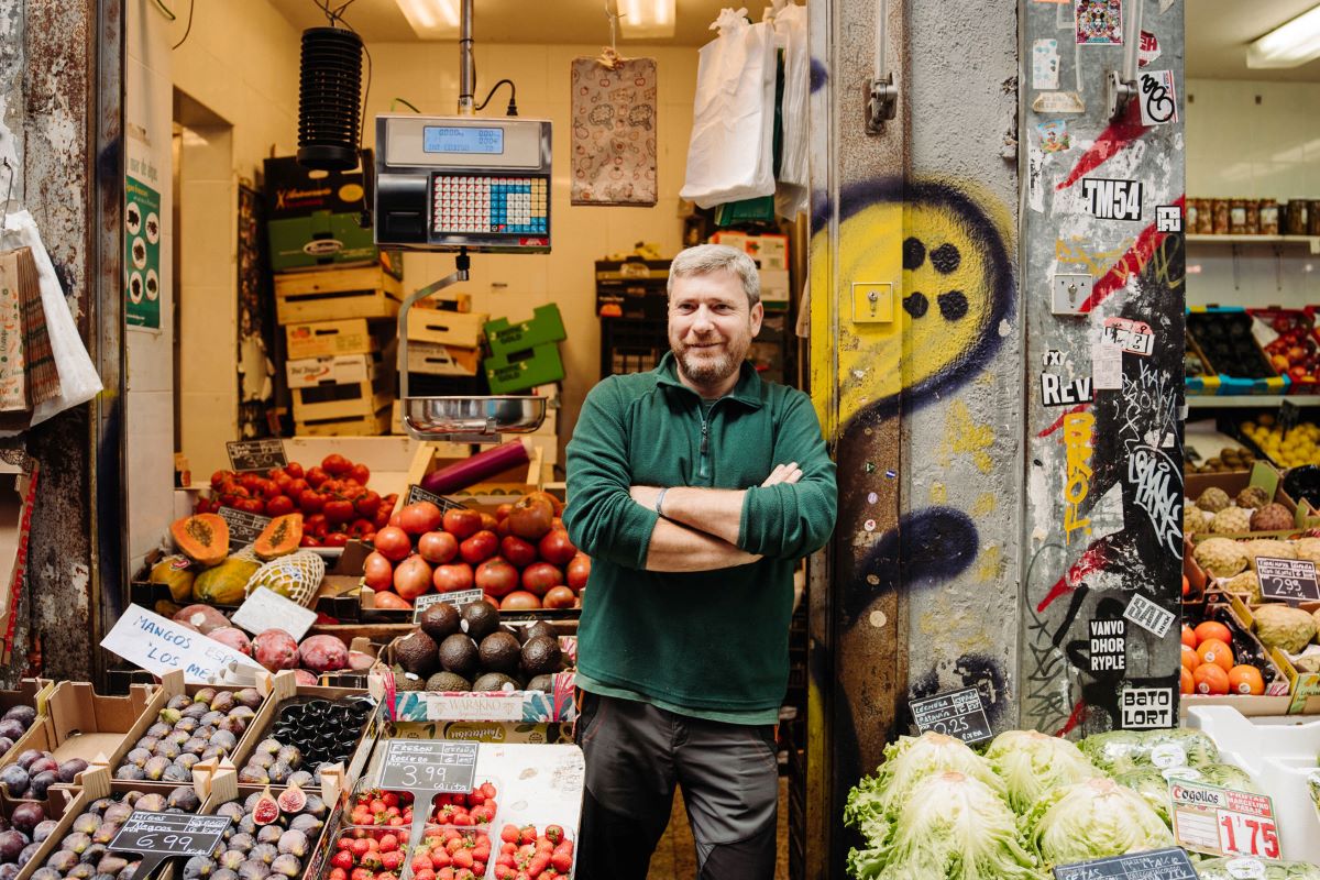 man in green shirt standing on wall in front of fruit stand